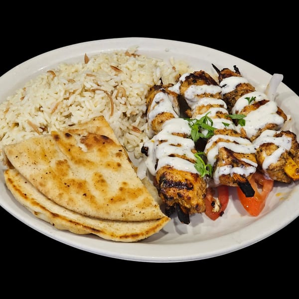Grilled chicken souvlaki skewers with tzatziki, rice pilaf, and pita bread on a white plate.
