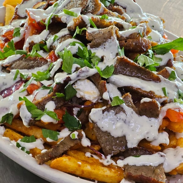 Close-up of Greek fries topped with gyro meat, feta, tomatoes, parsley, and tzatziki sauce.