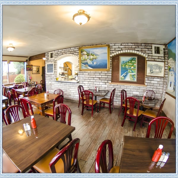 Interior of Firehouse Taverna, featuring wooden tables, red chairs, and Greek-themed artwork on brick walls.
