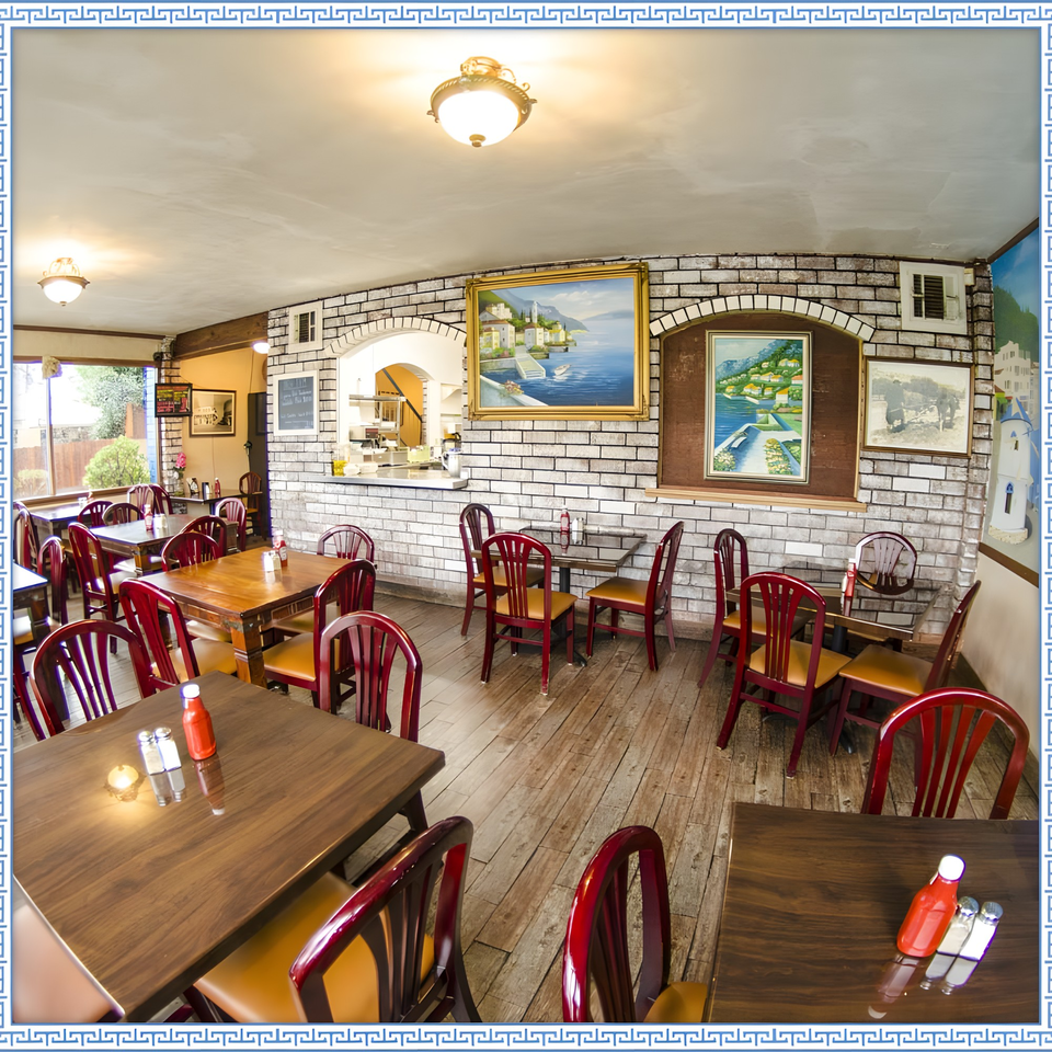 Interior of Firehouse Taverna, featuring wooden tables, red chairs, and Greek-themed artwork on brick walls.