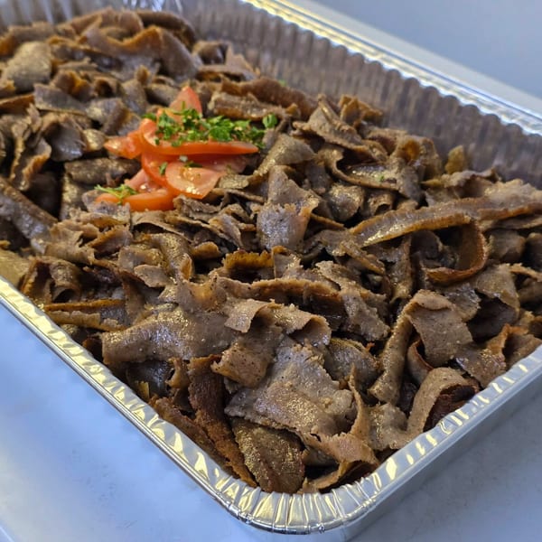 A large foil tray filled with sliced gyro meat, garnished with diced tomatoes and parsley.