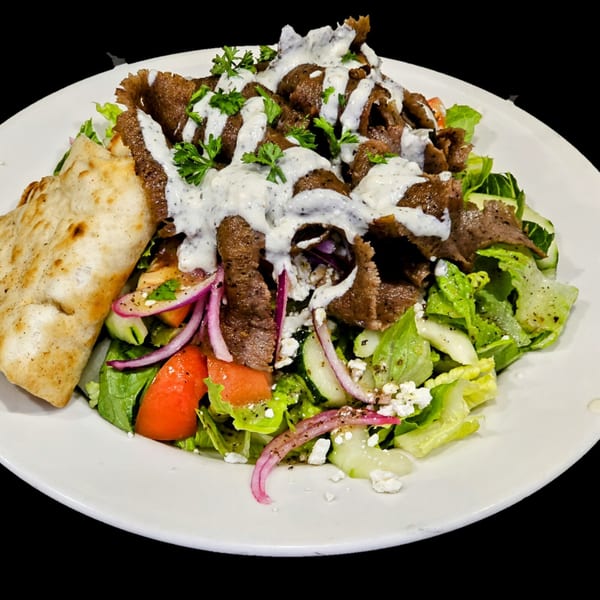 Greek gyro salad with sliced meat, lettuce, tomatoes, red onions, feta, tzatziki, and pita bread.
