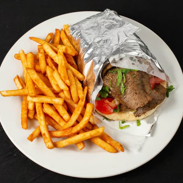 A Greek gyro wrapped in foil with tomatoes and parsley, served with a side of golden french fries.
