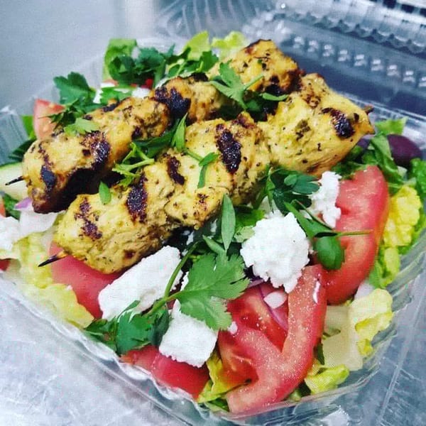 Grilled chicken skewers on a Greek salad with tomatoes, lettuce, olives, and feta cheese.