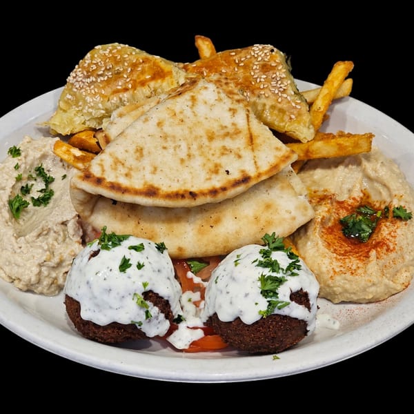 A Greek platter with falafel, pita bread, hummus, baba ghanoush, spanakopita, and french fries.