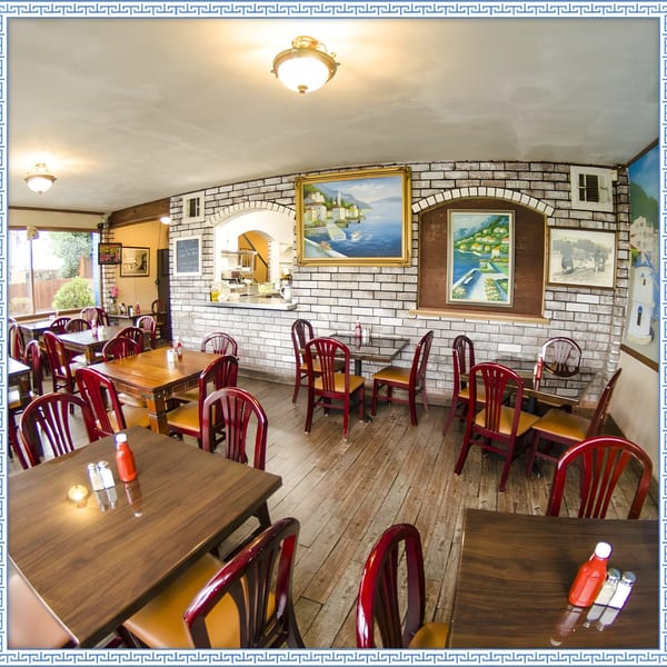 Interior of Firehouse Taverna, featuring wooden tables, red chairs, and Greek-themed artwork on brick walls.
