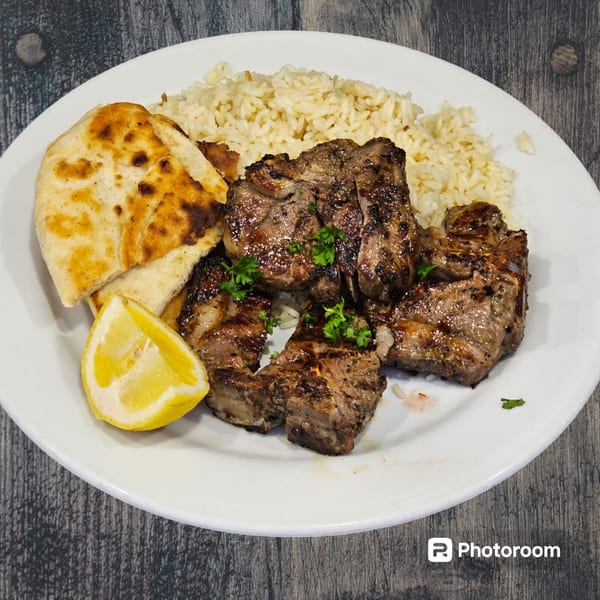 Grilled lamb chops with rice, pita bread, and a lemon wedge on a white plate.