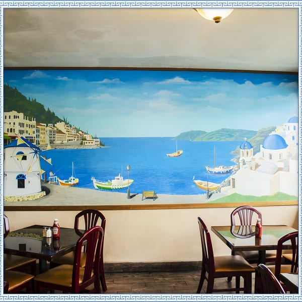 Restaurant interior with a large mural depicting a Greek coastal village scene with boats and windmills.
