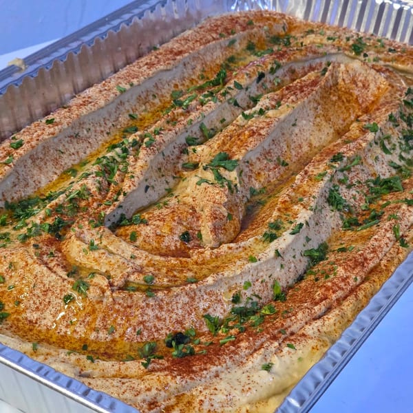 Large tray of hummus with paprika, olive oil, and parsley, ready for catering.