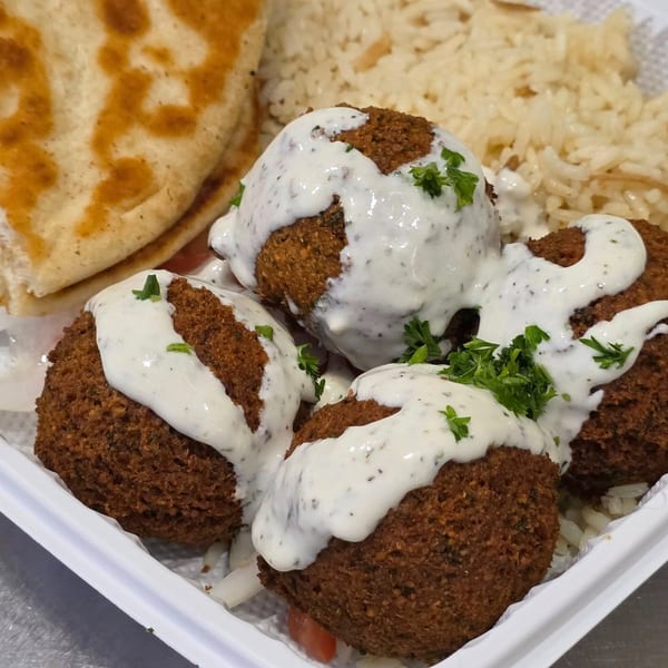 Four falafel balls topped with tzatziki sauce and parsley, served with rice and pita bread.