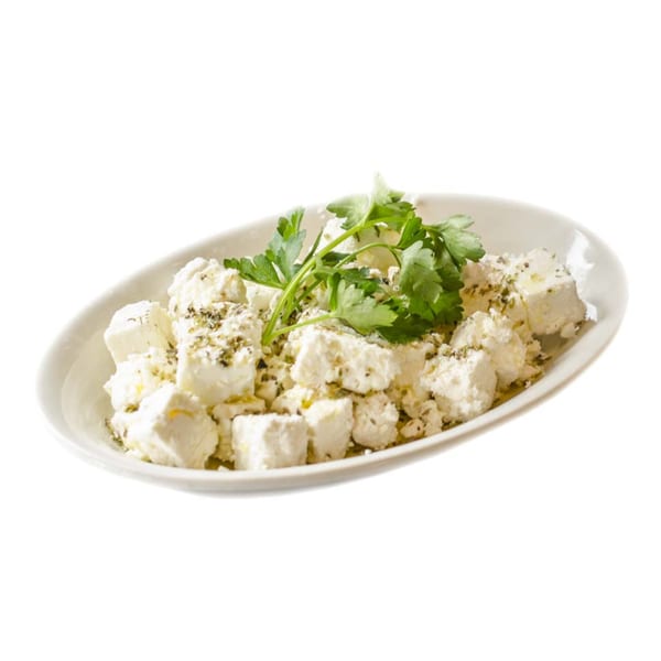 A white oval dish filled with cubed feta cheese, sprinkled with herbs and garnished with parsley.
