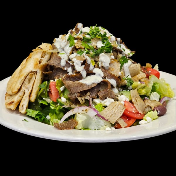 A large Greek gyro salad with meat, lettuce, tomatoes, feta, and pita bread.