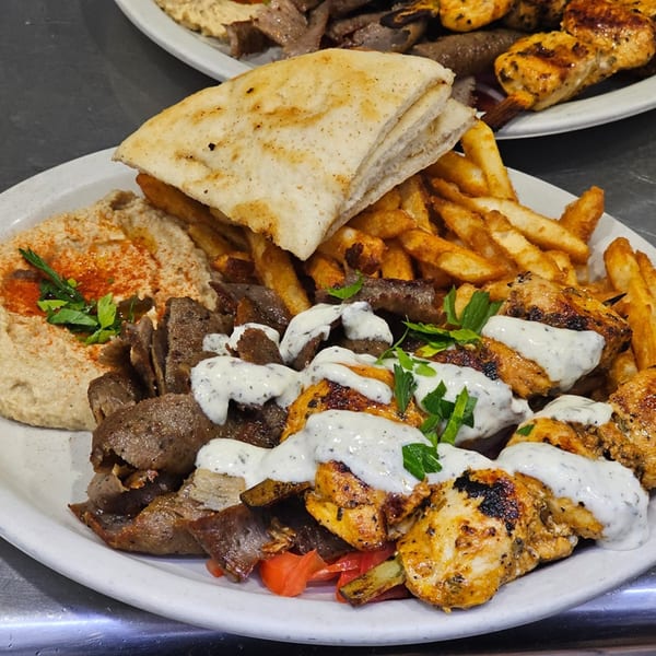 A Greek platter with gyro meat, chicken souvlaki, hummus, pita bread, and french fries.