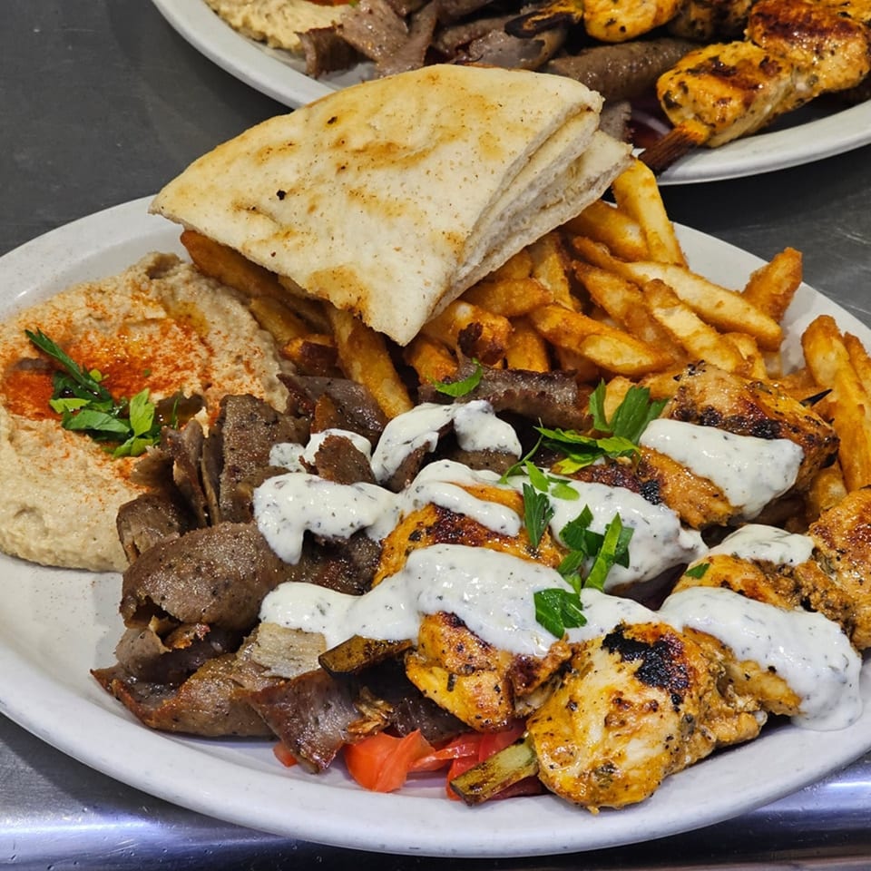 A Greek platter with gyro meat, chicken souvlaki, hummus, pita bread, and french fries.